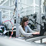 Engenheira trabalha em um laptop entre equipamentos tecnológicos avançados em um laboratório.