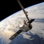 Satélite orbitando sobre a Terra, com formações de nuvens visíveis abaixo e o espaço ao fundo.
