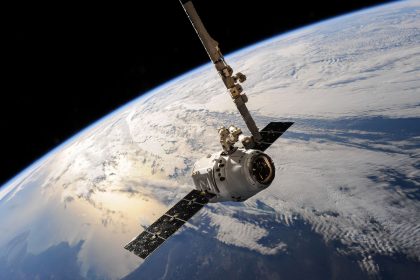 Satélite orbitando sobre a Terra, com formações de nuvens visíveis abaixo e o espaço ao fundo.