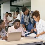 Equipe diversa colaborando em um projeto diante de um computador em um escritório moderno.