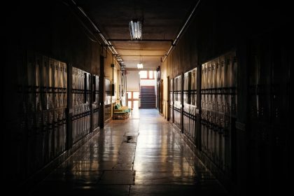 Corredor escolar escuro, com armários e uma fonte de luz ao fundo.