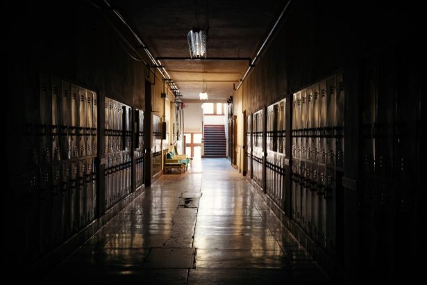 Corredor escolar escuro, com armários e uma fonte de luz ao fundo.
