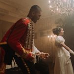Pessoas em trajes de época dançam em um salão de baile histórico.