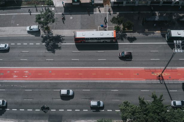 Vista aérea de uma via urbana movimentada, com carros, ônibus e ciclovias integrados ao sistema viário.